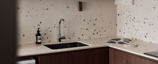 Playful modern retro kitchen design featuring dark wood cabinetry, terrazzo wall tiles, undermount sink, and quartz countertop.