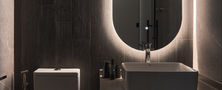 Luxury dark bathroom interior featuring floating dark cabinet vanity, white vessel basin, toilet, and backlit oval mirror.