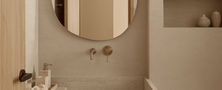 Close up detail of a custom carved beige stone block sink with dark wall mounted faucet fixture in a Light Resort Japandi home.