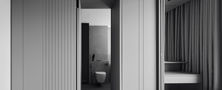Modern bedroom layout featuring subtle light grey vertical fluted panelling, vanity stool nook, and seamless ensuite bathroom access.