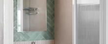 Stylish bathroom washbasin nook featuring sage green herringbone accent tiles, arched wall mirror, green vanity cabinet, and pendant light.