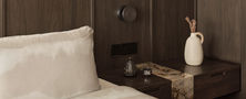 Dark Japandi bedroom bedside detail featuring white bedding dark wood wall panel integrated light and stone side table.
