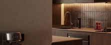 Dark Japandi kitchen counter view featuring dark grey textured tiles built in coffee bar and warm under cabinet lighting.