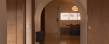 White arched doorway transition leading into a warm timber-panelled living space with soft ambient lighting.