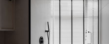 Clean Scandinavian shower area featuring black hardware, rainfall shower head, white wall tiles, and horizontal window blinds.