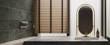 Organic Modern bathroom vanity counter featuring dual wall sconces, a stone sink basin, and natural light filtering through horizontal wooden blinds.