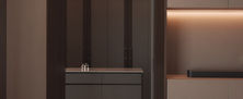 Minimalist dressing nook featuring integrated storage, soft backlit recess lighting, and a neutral ottoman stool.