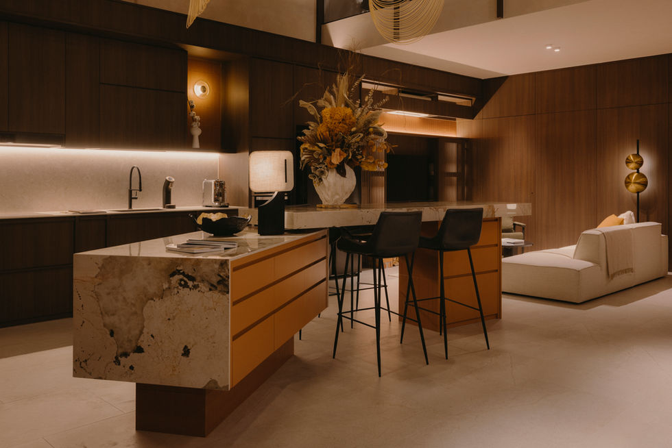 A monolithic stone kitchen island with a waterfall edge and matte black bar stools under architectural pendant lights.