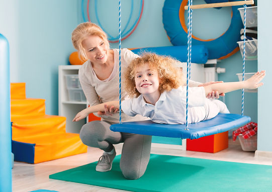 Woman helping a smiling boy to exercise on a therapy swing.jpg