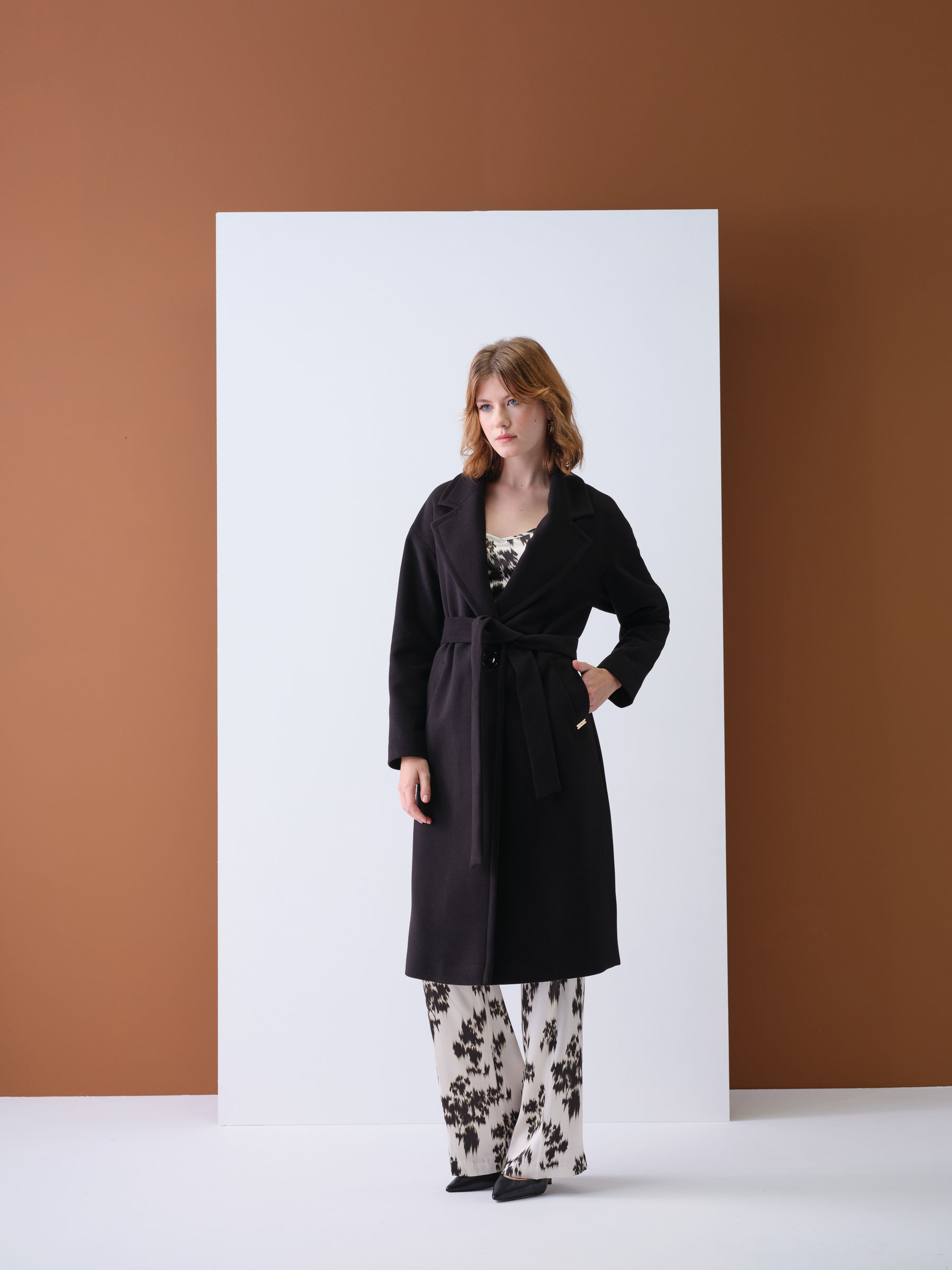 Uma mulher vestindo casaco preto e calça com estampa floral, exalando elegância e estilo.