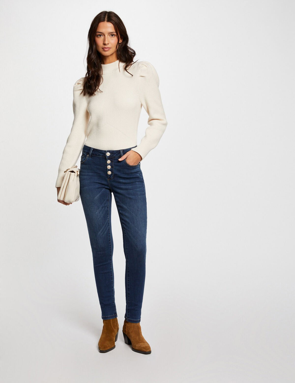 Os jeans skinny são azul escuro e têm botões na lateral. (Versão 1) Essa imagem mostra jeans skinny azul escuro com botões na