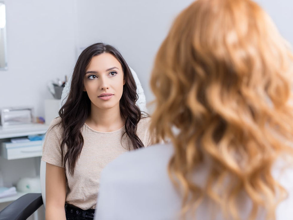 Woman with long dark hair listens attentively to another person with curly hair in an office. Neutral tones, calm setting.