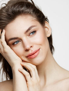 Smiling woman with long brown hair, resting her face on her hand. White background, natural makeup, serene expression.