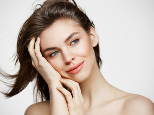 Smiling woman with long brown hair, resting her face on her hand. White background, natural makeup, serene expression.