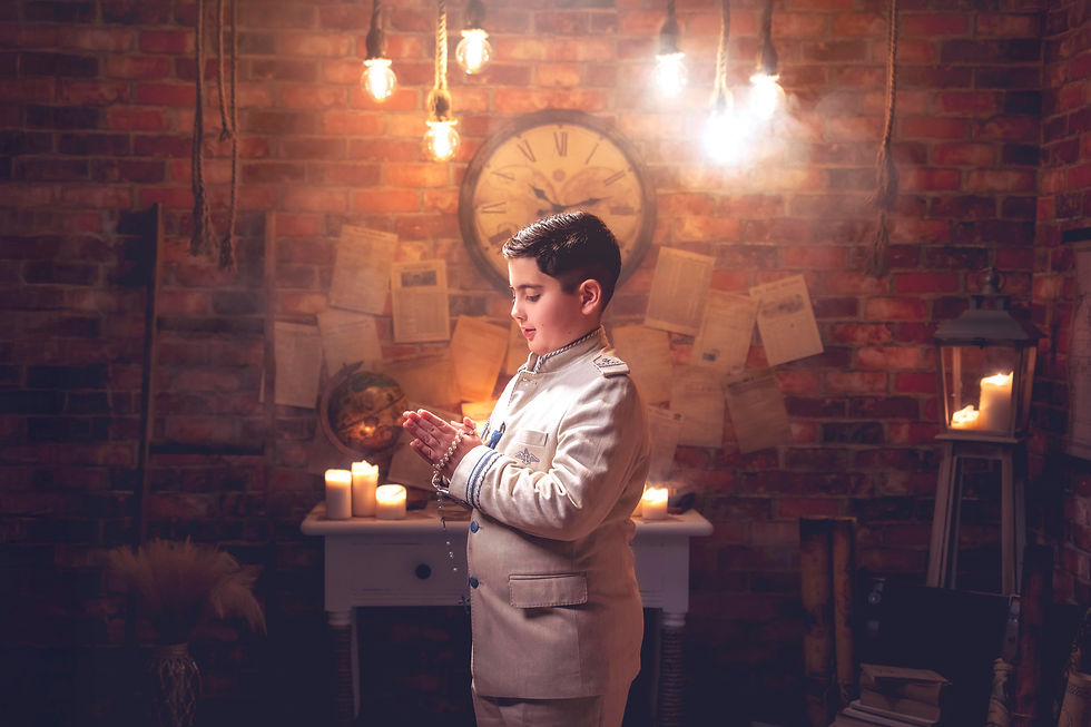 Fotografía de comunión en estudio Fradu Producciones en Adra, Almería. Niño con traje claro en escenario vintage con velas, reloj antiguo, globos terráqueos y luz cálida.