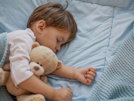"Toddler sleeping peacefully in bed hugging a teddy bear"