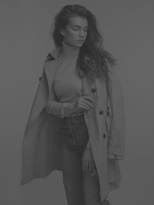 Woman wearing beige trench coat, standing in a studio. UK Fashion Boutique.