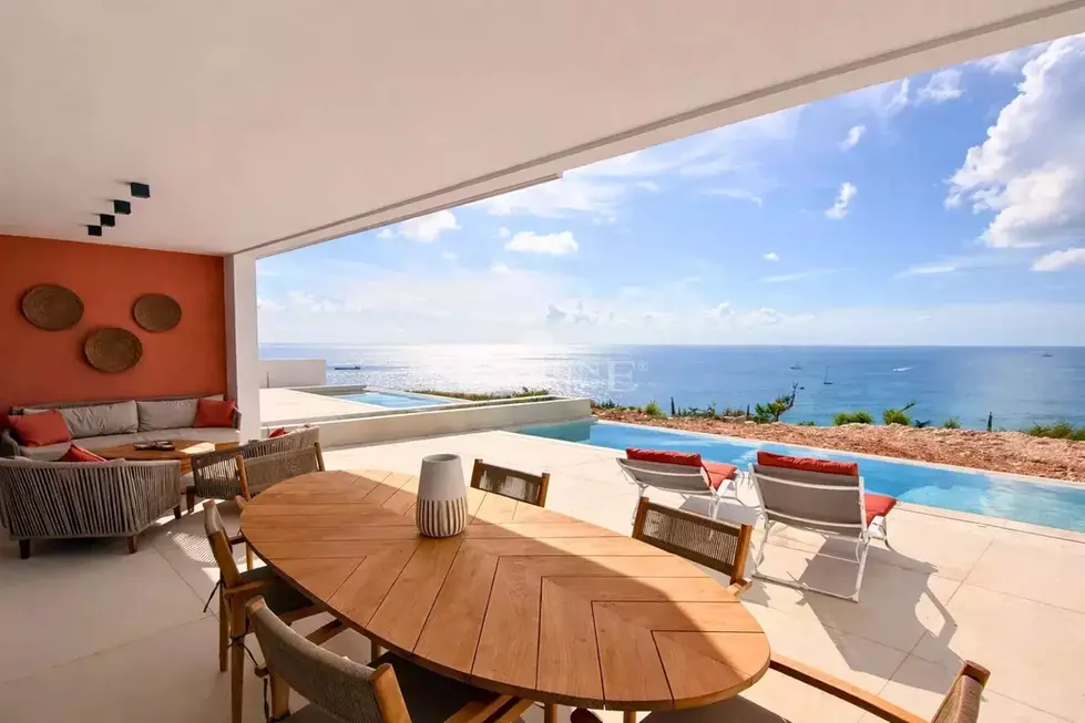 Outdoor dining area with terracotta accent wall and seating area in front of pool overlooking blue Caribbean skies and sea