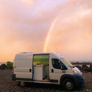 A Campervan Rental parked on the lava rock in front of a stunning rainbow.