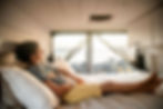 a girl laying in a Sun + Salt Campervan on Hawaii island with a palm tree, ocean, and lava rock in the background.