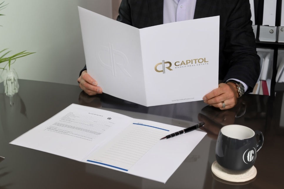 Man at desk holding white presentation folder with a gold logo and lettering.