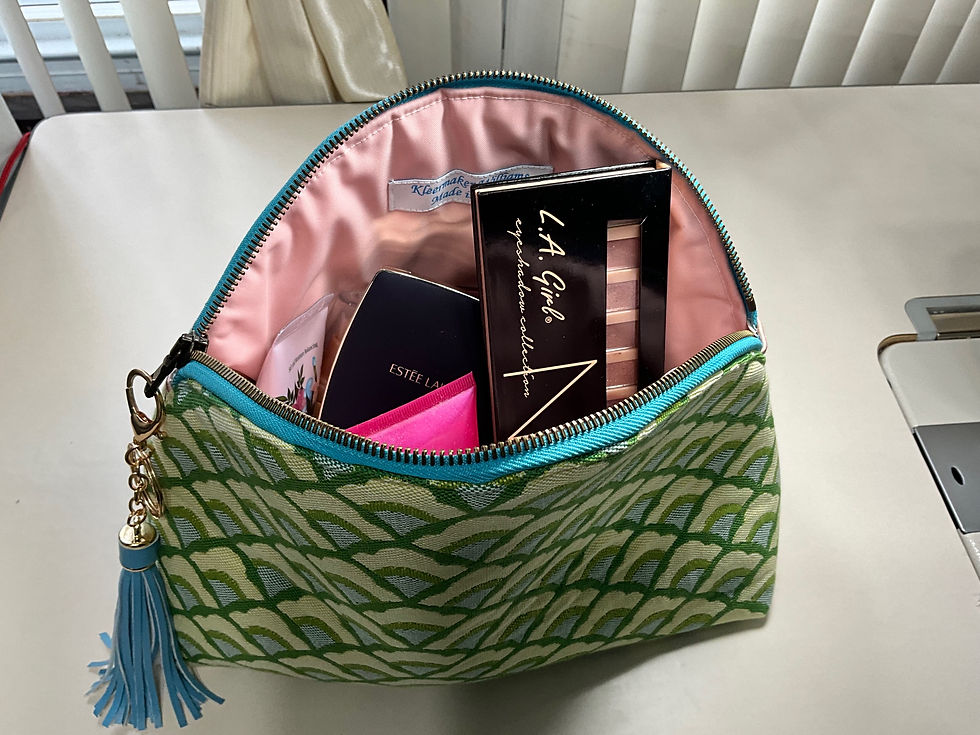 Thumbnail: “Open custom-made makeup bag with a green and blue scalloped pattern, showing a pink-lined interior holding various makeup items, including lipstick and a boxed product.”