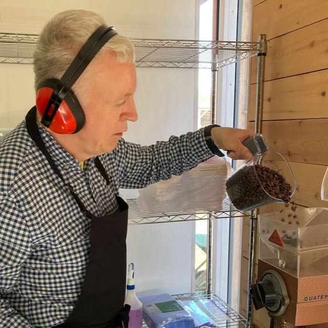 A man wearing ear defenders pouring coffee beans into a grinder