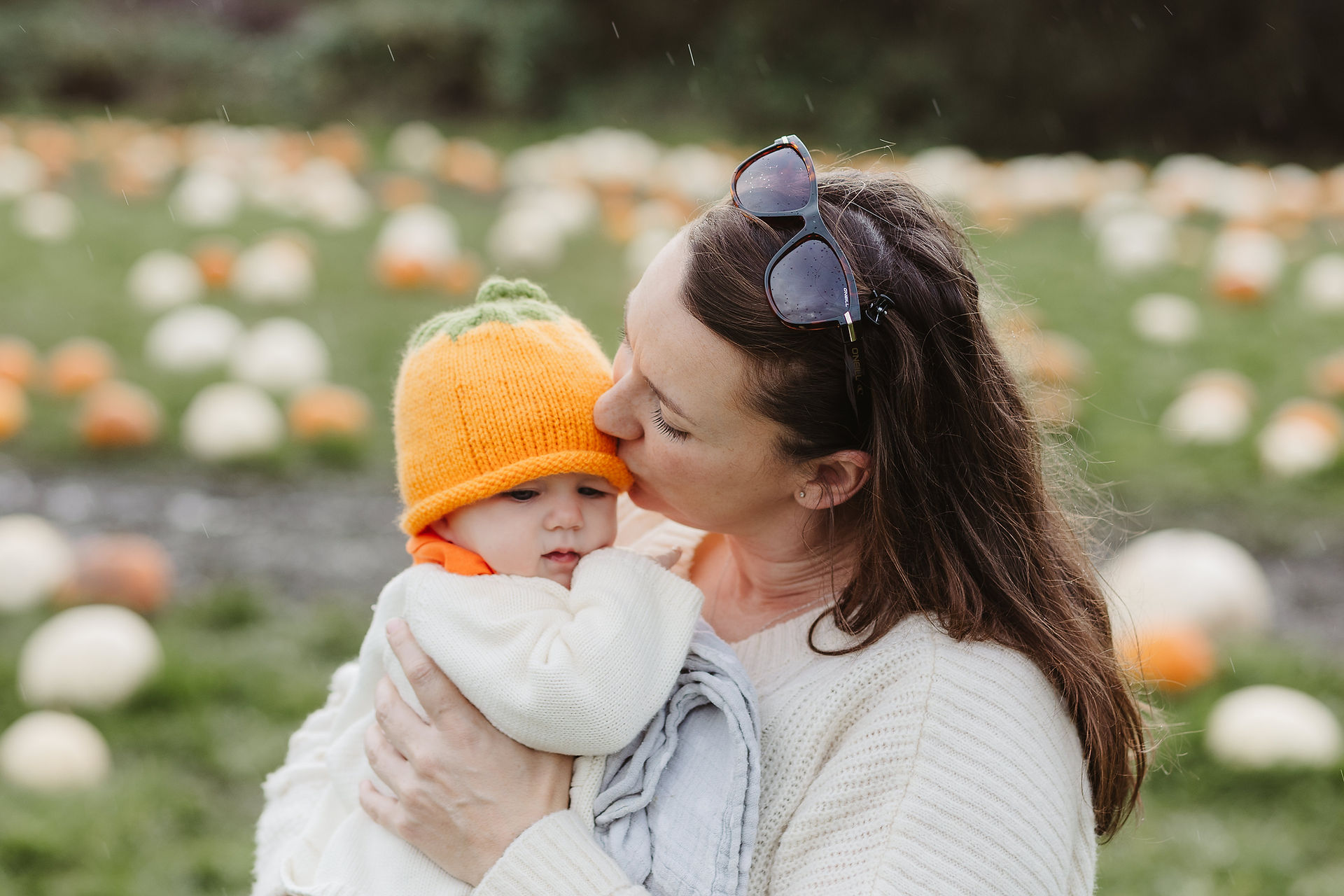 mother kisses her baby on the head in a pumpkin field