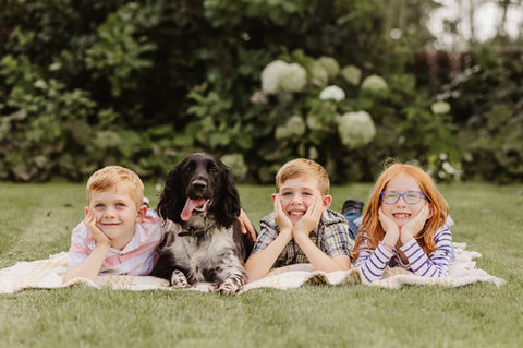 3 children and their dog pose for a photo laying on a blanket in the garden.