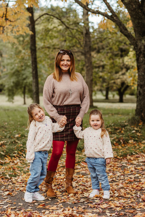 mum and her two daughters smile for the camera in the autumn leaves.