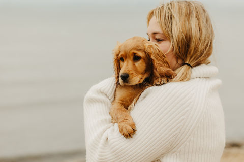 lady holds her puppy on the beach.