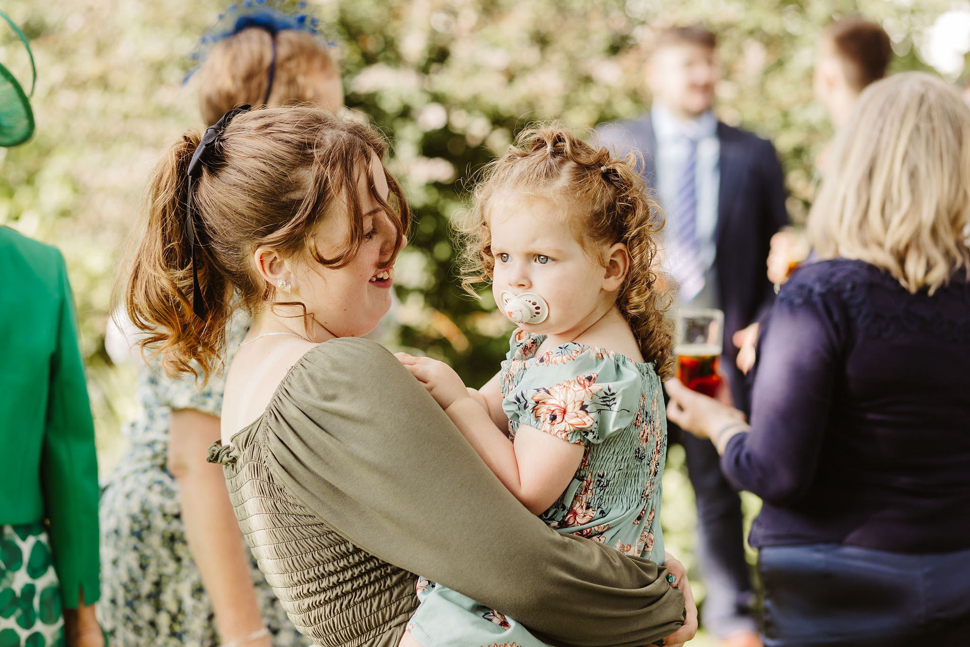 big sister holds little sister, dummy in mouth at wedding reception
