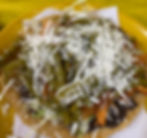 Corn tostada topped with shredded lettuce, cheese, green peppers, and shredded chicken on a yellow plate, set against a bright yellow background.