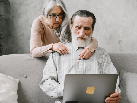 A mature couple sits together on a couch, reviewing their finances on a laptop to plan their future together.