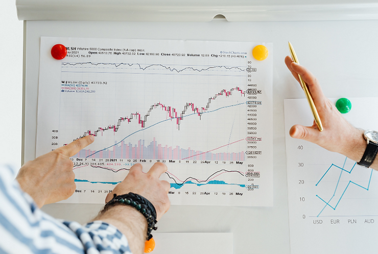 TWO PEOPLE POINTING AT A FINANCIAL MARKET CHART, REPRESENTING INVESTMENT STRATEGY AND FINANCIAL ANALYSIS.