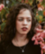 a woman in a black t-shirt with wavy hair standing in front of a flower bush