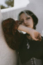 a woman with blue streaks in her hair and a septum ring poses with one arm lifted in a black blouse and waist cincher