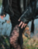 a woman wearing lacy black tights and a black skirt with a thigh slit and a leather jacket shown from the waist down in a grassy area