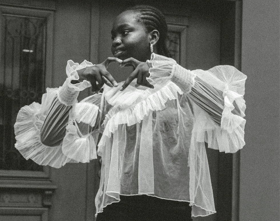 black and white photo of a young woman in a frilly white chiffon blouse making a heart with her hands