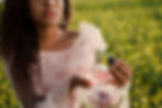 a woman in a field wearing a pink ruffled dress sprays perfume on herself