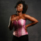 a woman in a pink corset and black pants posing in front of a black background.