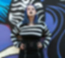 a woman with blue hair and a black and white striped sweater posing in front of a mural