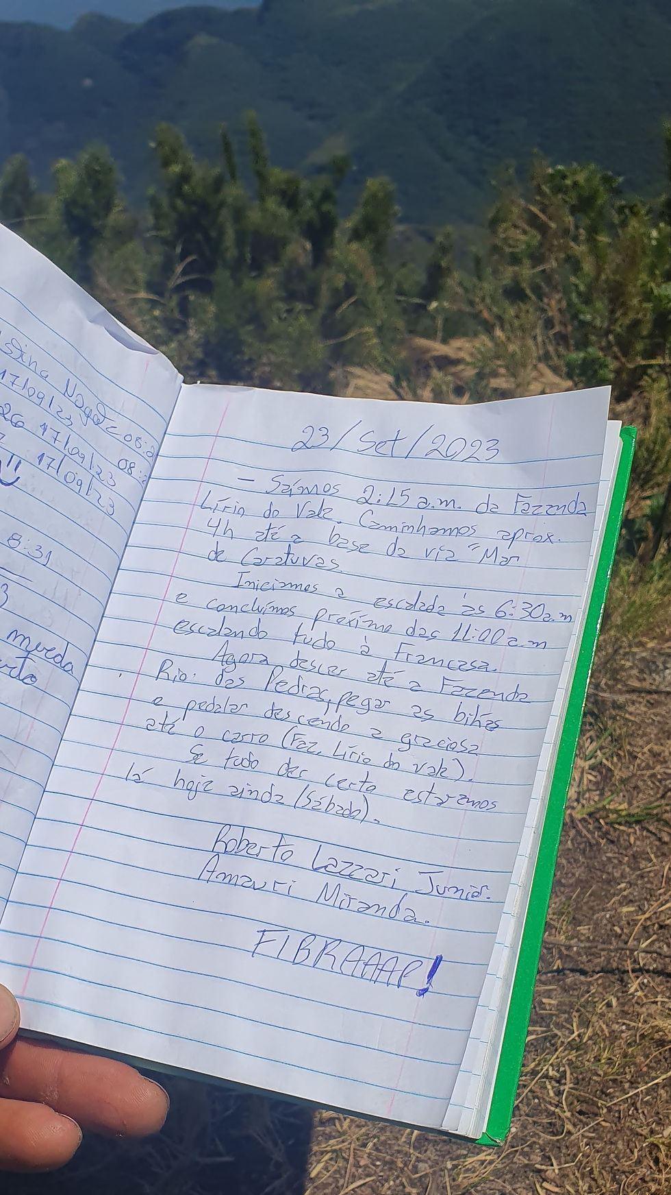 Caderno aberto com relato manuscrito detalhando uma escalada no dia 23 de setembro de 2023. Ao fundo, montanhas verdes e céu limpo.