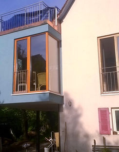 Der Anbau dient der Wohnraumerweiterung. Er setzt hier einen farblichen Akzent zum Bestandsgebäude und dient gleichzeitig als Balkon für das Dachgeschoss.