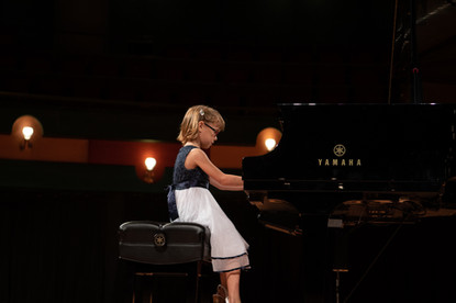 Young girl plays Yamaha piano during a recital on stage performance.