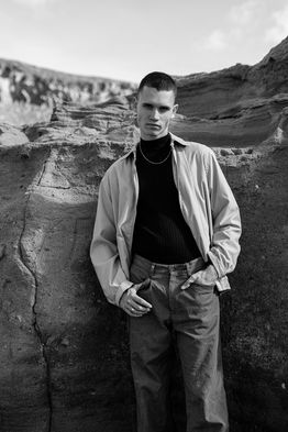 Outdoor portrait of male model Marco Santana wearing a light-colored jacket over a dark sweater and jeans.