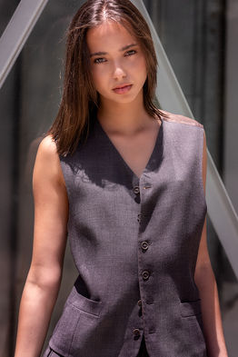 Model Idaira Herrera posing outdoors in a matching suit vest and trousers with a glass elevator mechanism in the background.