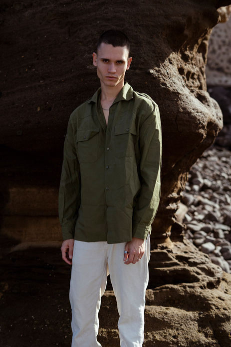Outdoor portrait of male model Marco Santana wearing an unbuttoned green shirt over light-colored trousers.
