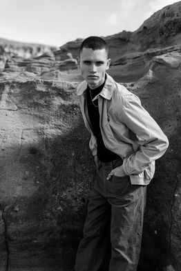 Outdoor portrait of male model Marco Santana wearing a light-colored jacket over a dark sweater and jeans.