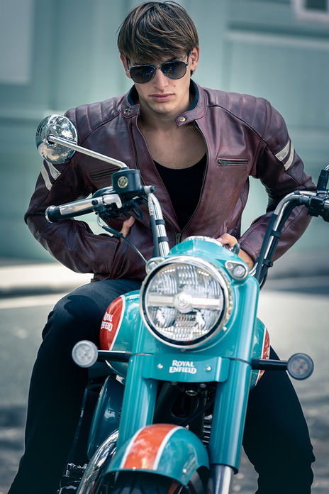 Leonardo Russo new face male model wearing a burgundy leather jacket with white stripes riding a Royal Enfield motorcycle with Prada aviator sunglasses Salitre Models
